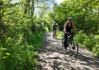 Imagined use of Brixham Railway Heritage Trail - 2 cyclists riding along trail bordered by green vegetation and trees
